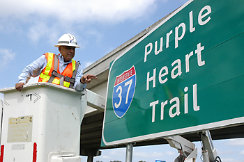 Albert Perez helps install a Purple Heart Trail sign on I-37 at the Oakville overpass.